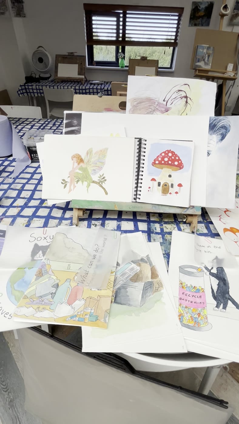 Sketchbook and finished character illustrations laid out on the workshop table