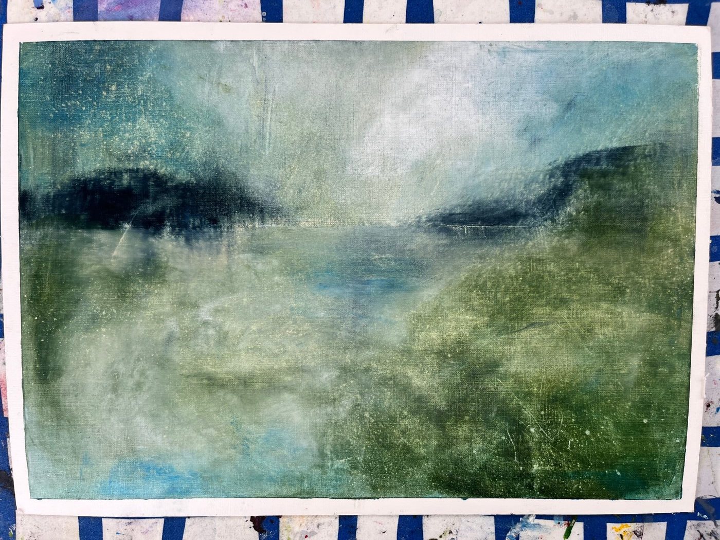 A misty cold wax landscape in greens and blues, a dark headland across the middle