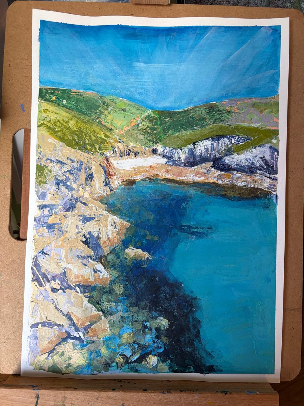 Kat’s acrylic of a Cornish cove: turquoise and deep blue water, pale rocks, green headland under a blue sky