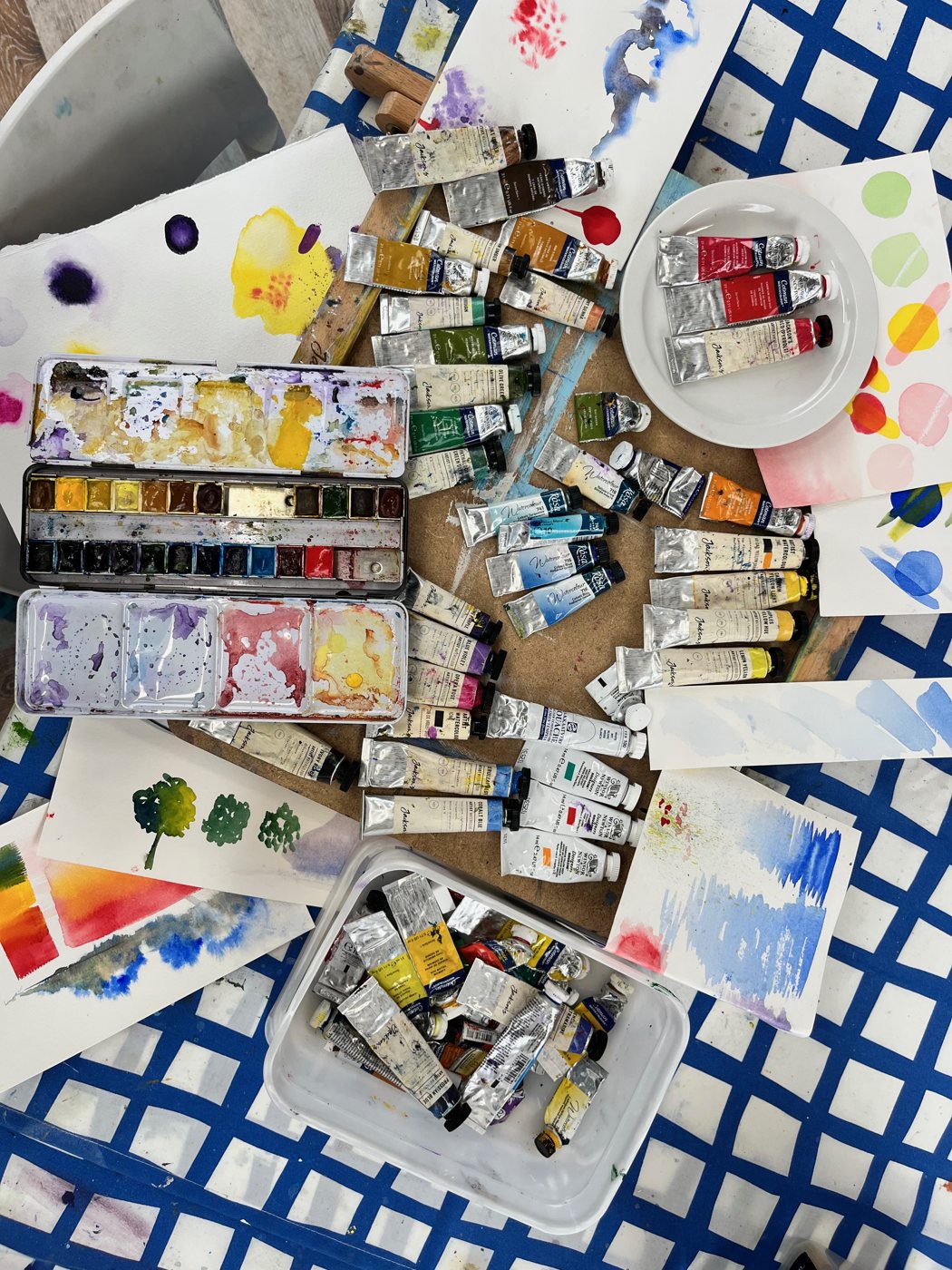 Paint tubes, pans and palettes spread across the table