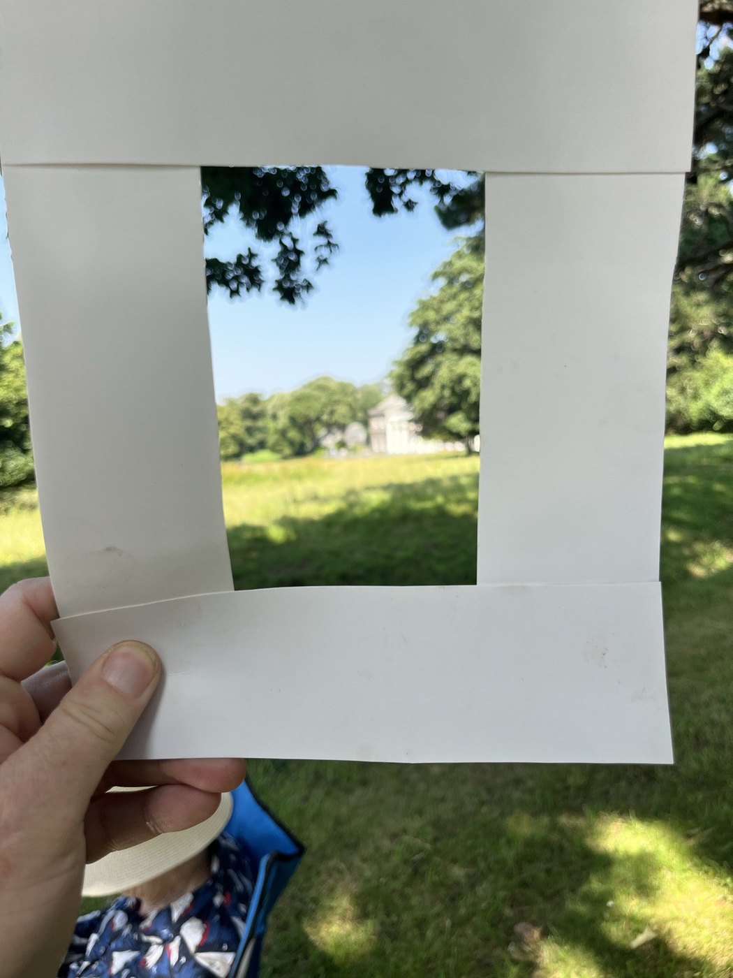 A hand holding a cut paper viewer frame up against the landscape
